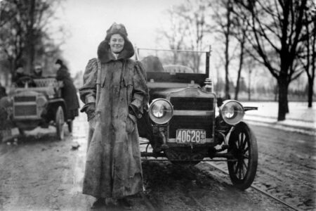 A woman in a coat showing well-being next to a car.