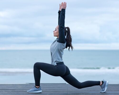 Una mujer haciendo sentadillas frente al océano para promover el bienestar y el fitness.