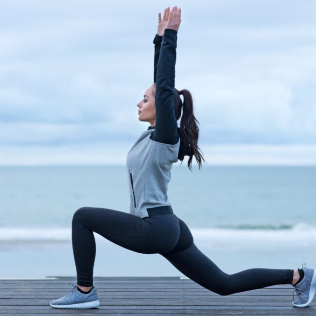 Una mujer haciendo sentadillas frente al océano para promover el bienestar y el fitness.